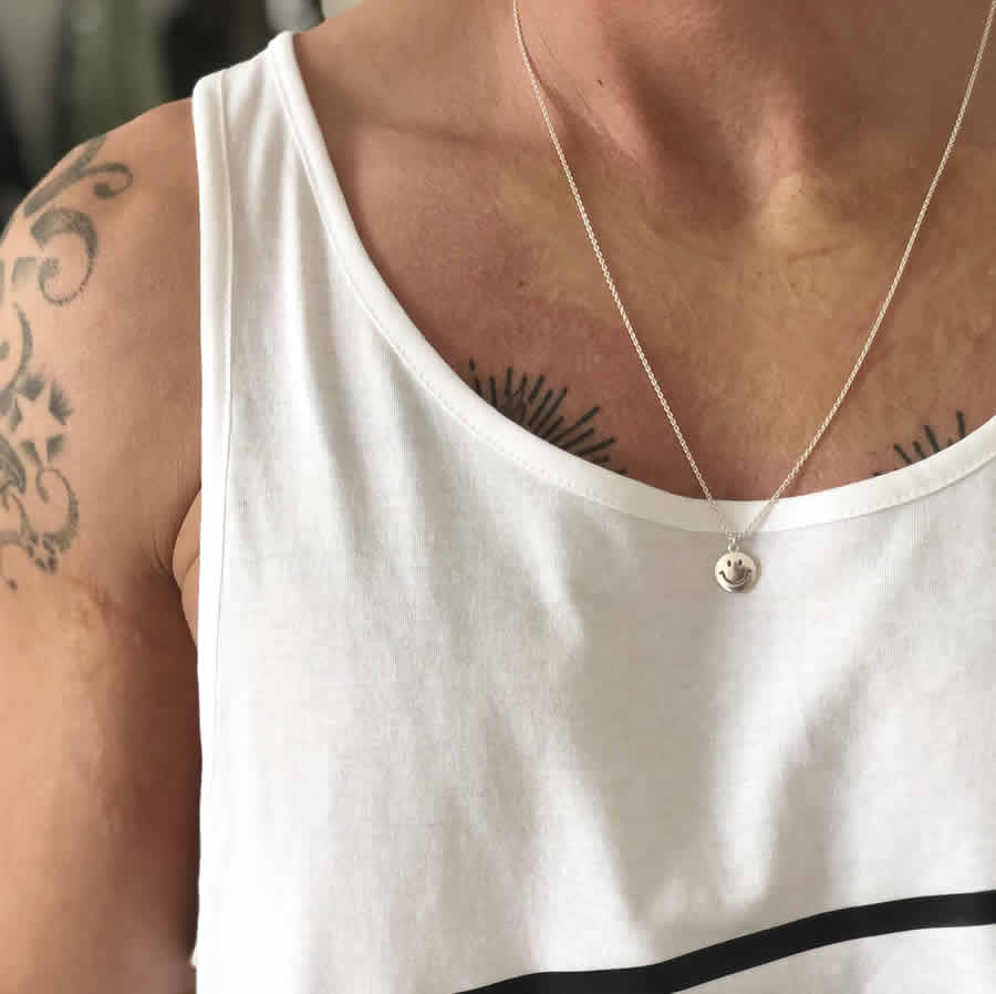 Smiley face necklace worn with streetwear and layered jewelry