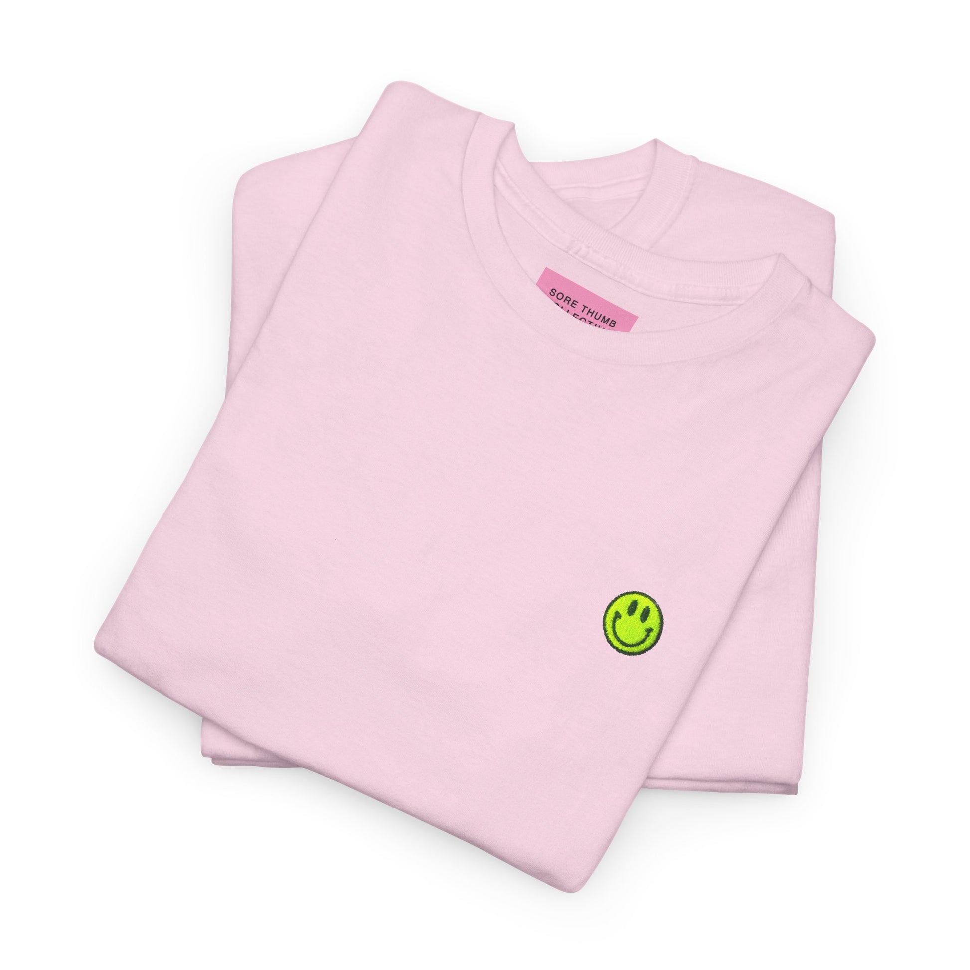 Folded pink t-shirt with a green smiley face logo on a white background